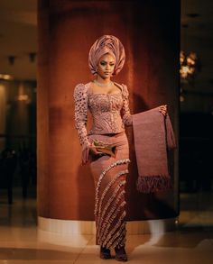 a woman standing in front of a tall pillar wearing a pink dress and head scarf