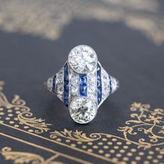 One of the most unique interpretations of one of the most enduring and romantic motifs in jewelry: the Toi et Moi ("You and Me"). Two diamonds are bezel set vertically and accented by calibre-cut sapphires, adding just the perfect splash of color as the sapphires also run vertically across the top of the ring. Both diamonds (we actually love how the diamonds are not perfectly matched - perhaps a deliberate choice by the original jeweler, or the person who originally commissioned the piece, repre Modern Mens Rings, Art Jewelry Earrings, Splash Of Color, Antique Watches, Antique Engagement, Vintage Band, The Ring, Men's Rings, Vintage Engagement Rings