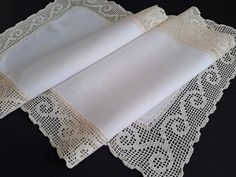 two white placemats with lacy doily on black table cloth, one folded and the other closed