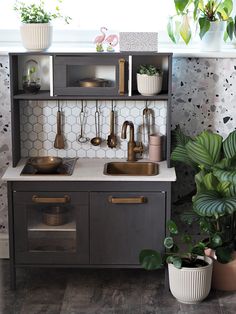 a small kitchen with plants and pots on the counter top in front of the sink