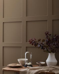 a table topped with plates and bowls next to a vase filled with flowers on top of a wooden table