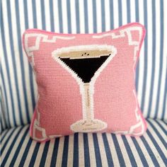 a pink and white pillow with a martini glass on it's side, sitting on a striped couch