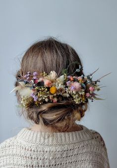 the back of a woman's head wearing a flower crown with feathers and flowers on it