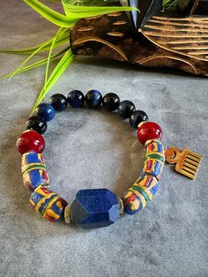 Kente Chief Lapis Lazuli, Blue Tiger eye, Deep Burgundy glass beads, & Krobo Recycled Glass beads  Men's/Unisex Bracelet  ------------------------------------- Like royalty, this bracelet invokes the indomitable spirit of kings of ancient West African empires. The recycled Krobo glass beads are patterned in the striated  deep rich hues of handwoven Kente cloth The chatoyancy of the 12mm premium AAA blue tiger eye gemstone beads is breathtaking, along with the beauty of 14mm deep burgundy glass b Adjustable Blue Stretch Bracelet With Wooden Beads, Artisan Blue Beaded Bracelets With Round Beads, Blue Wooden Beads Stretch Bracelet As Gift, Blue Wooden Beaded Bracelets As Gift, Adjustable Blue Beaded Bracelets With Wooden Beads, Blue Wooden Beads Stretch Bracelet, Blue Stretch Bracelet With Round Wooden Beads, Artisan Blue Beaded Bracelets As A Gift, Artisan Blue Beaded Bracelets For Gift