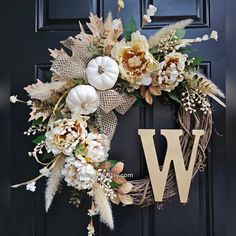 a wreath that has the letter w on it and flowers hanging from it's front door