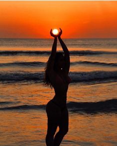 a woman standing on top of a sandy beach next to the ocean holding a frisbee