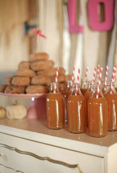 there are many bottles with straws in them on the table next to donuts