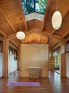 an empty room with wooden floors and two lamps hanging from the ceiling, along with yoga mats on the floor