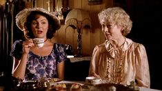 two women sitting at a table with tea cups in their hands and plates on the table