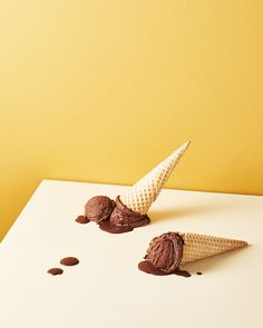 two scoops of ice cream sitting on top of a white table next to a yellow wall