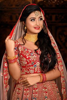 a woman in a red and gold bridal outfit with her hands on her hips