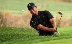 a man in black shirt and hat playing golf on green grass with ball coming out of hole