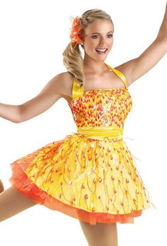 a woman in a yellow and orange dress with her arms out, smiling at the camera