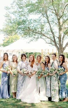 a group of women standing next to each other in front of a tree and grass field