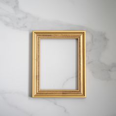 an empty gold frame on a white marble wall