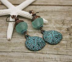 MYKONOS GREEN PATINA SAND DOLLAR AND AQUA AFRICAN GLASS EARRINGS Greek Sand Dollar charms dangle beneath African glass beads in aquamarine.  A shell shaped copper bead cap tops the glass. Sensitive ears? Hypoallergenic niobium earwires in antique brass with a copper ball. Great gift for your favorite beach lover!  2 1/2 inches View more She Shellz Earrings here: https://www.etsy.com/shop/SheShellzByCaptDeb?ref=seller-platform-mcnav&section_id=14171400 Thanks for cruising with Captain Deb! Turquoise Wire Wrapped Earrings For Beach, Summer Beach Earrings With Wire Wrapped Detail, Summer Beach Wire Wrapped Earrings, Handmade Beachy Green Jewelry, Green Dangle Jewelry For The Beach, Green Drop Earrings For Beach, Green Drop Earrings For The Beach, Green Jewelry With Matching Earrings For The Beach, Green Beachy Jewelry For Vacation