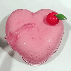 a pink heart shaped cake with a cherry on it's top, sitting on a white surface