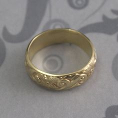 This ring is a statement in itself! Hand forged from 6.5mm wide by 1.5mm thick solid 14K gold stock that has been embossed with a floral/swirl design, this ring will be made to size just for you and given a high polished finish. Please note that the white and rose gold options can take a little longer because they must be cast using the lost wax method rather than fabricated from patterned gold stock. Blazer Arts is a family-owned and operated small but growing business that first opened up shop Heirloom Gold Carved Ring, Heirloom Style Carved Gold Rings, Heirloom Carved Gold Rings, Yellow Gold Carved Rings For Anniversary, Carved Yellow Gold Rings For Anniversary, The Garden Band, Art Nouveau Ring, Growing Business, Flower Band