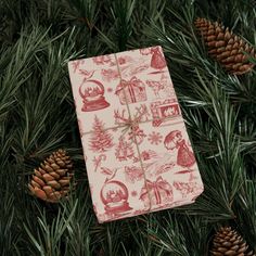 a present wrapped in red and white wrapping paper on top of pine branches with cones