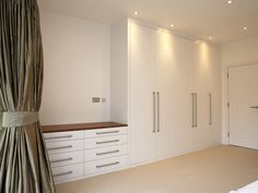 an empty bedroom with white cabinets and drawers in the corner, next to a curtained window