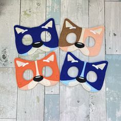 three masks with different colors and shapes on a wooden floor, one has a cat's face