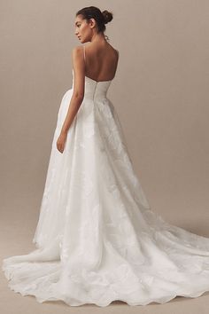 a woman in a white wedding dress looking down at the back of her gown,