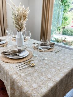 a table set with place settings and silverware in front of a window overlooking a garden