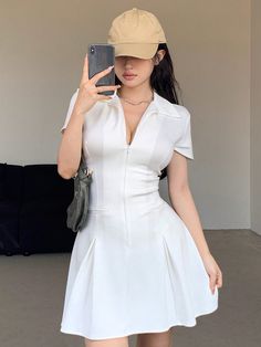 a woman taking a selfie in a white dress and tan hat with her cell phone