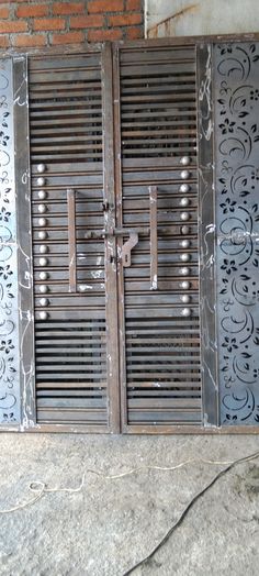 two metal doors with intricate designs on the side of a brick wall next to a concrete floor