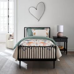 a bedroom with a bed, nightstand and heart shaped mirror on the wall above it