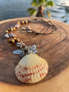 This necklace has been handcrafted on a beautiful espresso leather. This scallop seashell is from the shores of the FL Panhandle. It has been adorned in petite swarovski crystals and accents. The shell has been coated with a resin and charms have also been added. The charms are oxidized silver metal which gives this necklace a vintage appeal. (Charms include a cross, large and small ovals , and a flower). The necklace is double strand and has jasper gemstones, silver metal accents, and petite foil glass beads.   The length of the necklace is a total of 28 inches in the neck area (14 each. side). The shell is 2 inches wide. This is the perfect necklace to slip on and off over the head. No clasps to fasten.  The necklace ties at the neck area and the tassel ends have petite beads and silver Bohemian Brown Shell As Gift, Handmade Brown Shell-shaped Necklace, Handmade Brown Shell Necklace, Bohemian Brown Shell-shaped Jewelry, Handmade Brown Shell-shaped Jewelry, Handmade Brown Shell Jewelry, Bohemian Brown Shell Jewelry, Nickel-free Brown Jewelry For The Beach, Handmade Bohemian Brown Shell