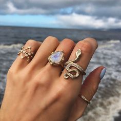 a woman's hand with three rings on it and the ocean in the background