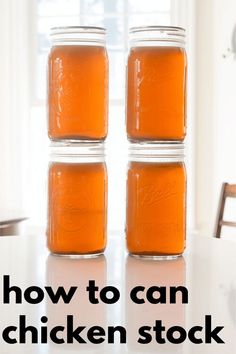 three jars filled with orange liquid sitting on top of a table next to a window