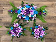 purple and blue flowers are arranged on a wood floor with greenery in the center