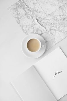 a cup of coffee on top of a white table next to a notebook and pen