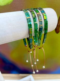 "These handmade mixed green ombre Tila bead bracelets are constructed with GENUINE Miyuki beads and woven on superior waxed cord. These gorgeous green and gold beaded bracelets are COMPLETELY ADJUSTABLE! You have the option of wearing these beauties loose OR snug. STERLING SILVER ball-ends add just the right amount of sparkle as they swing from your wrist, and with just a gentle pull on each end these bracelets adjust to your ideal fit. Perfect for teacher appreciation gifts, everyday wear, yoga Tila Bead Bracelets, Square Bracelet, Seed Bead Crafts, Green Beaded Bracelets, Friendship Bracelets With Beads, Miyuki Bracelet, Bracelet Minimalist, Bracelet Display, Strung Beads