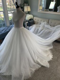 a white wedding dress is on display in a living room with a couch and large windows