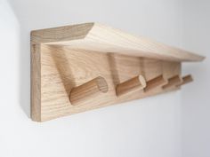 a wooden shelf mounted to the side of a wall with three pegs on it