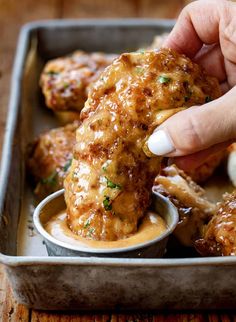 a person dipping sauce on some chicken wings