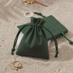 a green bag sitting on top of a sandy beach next to two gold bracelets