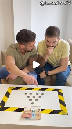 two men sitting at a table making a cutout out of a construction paper board