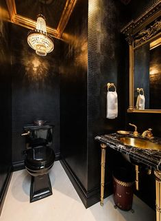 a black and gold bathroom with chandelier above the toilet, sink and mirror