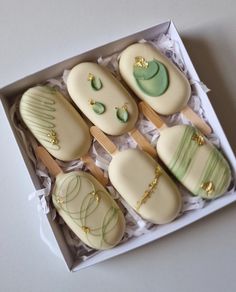 six decorated cookies in a box with wooden spoons on the top one is green and white