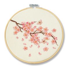 a cross stitch pattern with pink flowers on white fabric, in a wooden hoop hanging from the wall