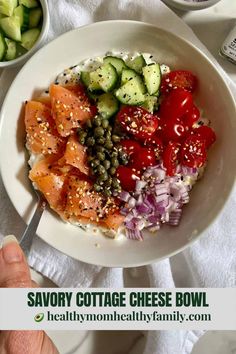 a white bowl filled with salmon, cucumbers and tomatoes on top of a table