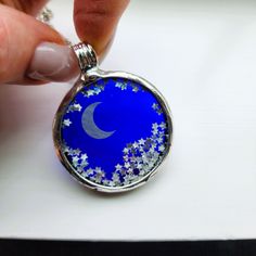 The celestial shaker necklace for women is a unique and mesmerizing piece, perfect as a gift for your daughter. This beautiful fidget necklace features a moon and stars pendant with free moving stars inside, offering both elegance and a calming, interactive experience. Crafted with delicate stained glass jewelry elements, the necklace captures light beautifully, making it a truly enchanting accessory. Pocket watch crystals are durable and make the perfect glass in which to encase small things. This one is combined with cobalt blue stained glass. Encased is a silvery moon with small stars that move freely Fun! Check out the video.   * Fidget Necklace * Pendant: 2 inch H x 1 1/2 inch W * Shiny Silver Finish * Truly Hand Made in USA at Bayou Glass Arts Studio * Ready to ship * Expedited Shipp Magical Star-shaped Jewelry For Gifts, Magical Star-shaped Jewelry Gift, Mystical Star Charm Jewelry Gift, Whimsical Star Charm Jewelry As Gift, Mystical Star Charm Jewelry For Gift, Whimsical Star Charm Jewelry Gift, Mystical Jewelry With Star Charm For Gifts, Mystical Star-shaped Necklace For Gift, Mystical Star-shaped Jewelry Gift