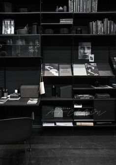 a black book shelf filled with lots of books next to a chair and table in front of it