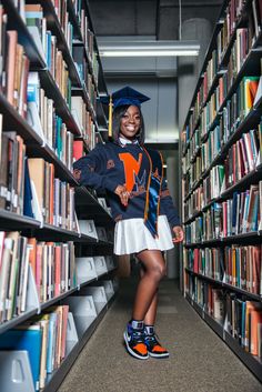 a woman in a graduation cap and gown standing next to a book shelf filled with books