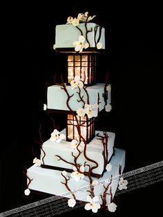 a three tiered cake with white flowers and branches on the top is lit up at night