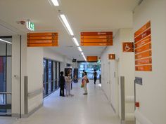 several people are walking down the hallway in an office building with orange and white signs